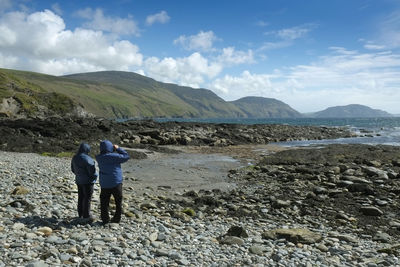 Rear view of friends standing on shore against sky