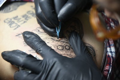 Cropped hand of artist drawing tattoo on customer body