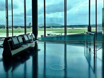 Empty chairs and tables against sky seen through window