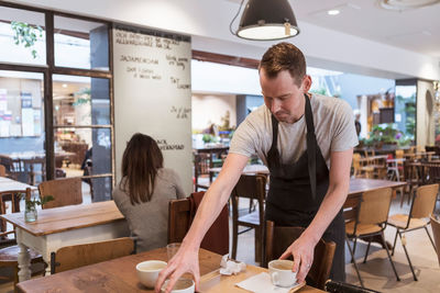 Male owner with coffee cups at table in cafe