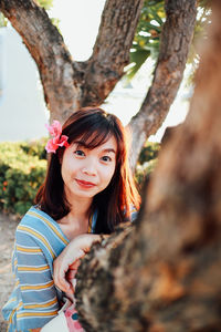 Portrait of smiling young woman against tree trunk