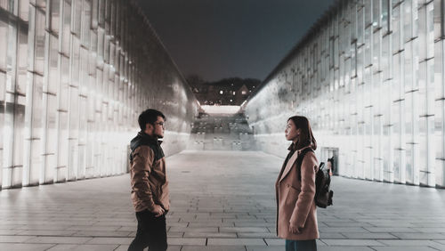 Couple standing on footpath in city at night