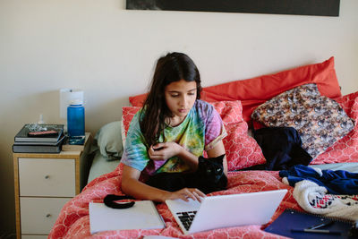 Tween girl with her black cat does schoolwork in bed on her laptop