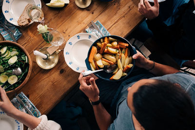 High angle view of man holding utensil of potatoes and carrots while sitting with friends