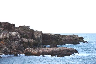 Rock formation by sea against clear sky