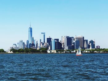 Sailboats in city by buildings against clear sky