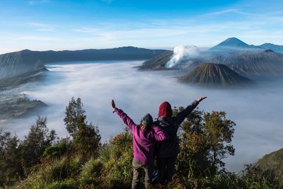 Rear view of people standing on mountain against sky