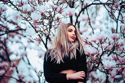 Low angle view of young woman standing against flowering tree