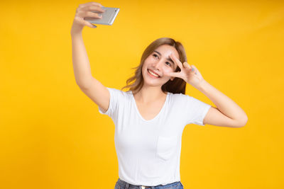 Portrait of smiling young woman using mobile phone against yellow background