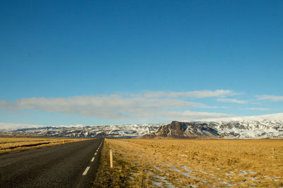 Road leading towards snowcapped mountains against sky