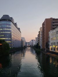 Buildings by river against sky during sunset