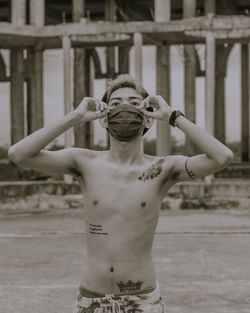 Shirtless young man wearing flu mask standing outdoors