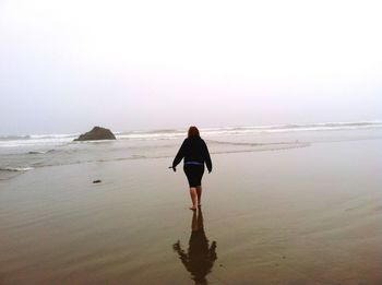 Rear view of woman standing on beach against clear sky