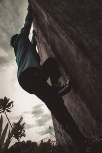 Low angle view of man climbing rock against sky