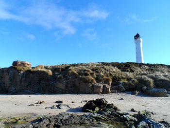 Lighthouse at beach against sky