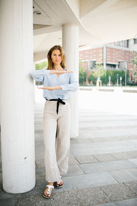 Portrait of young woman gesturing equal sign while standing by column