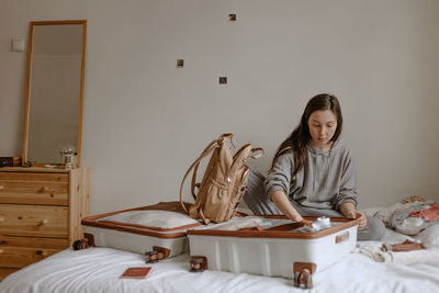 Young woman with open suitcase on the bed at home