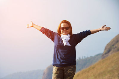 Young woman with arms raised standing on landscape against sky