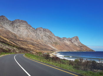 Road by mountain against clear blue sky