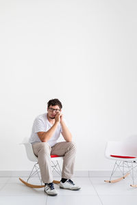 Young man sitting on chair against white background