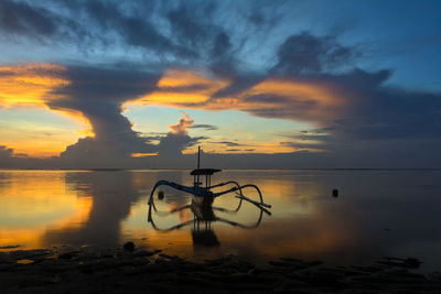 Silhouette bicycles on beach against sky during sunset