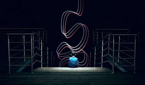 Digital composite image of boy sitting by light painting on staircase at night