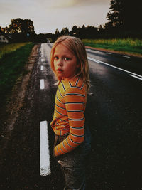 Portrait of boy standing on road against trees