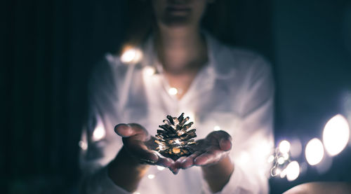 Midsection of woman holding illuminated pine cone in darkroom