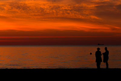 Silhouette people standing on shore against sky during sunset