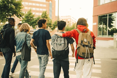 Rear view of male friends crossing road side by side in city