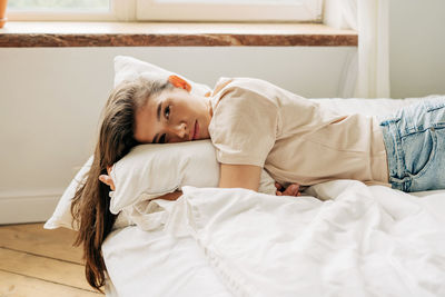 Young sad melancholic brunette woman lying on the bed looking at the camera.