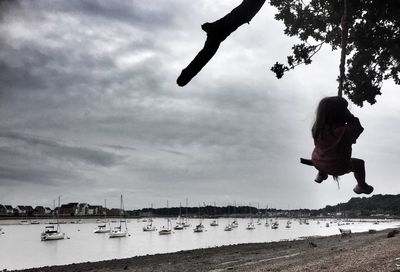 Full length of playful girl swinging on rope swing at harbor