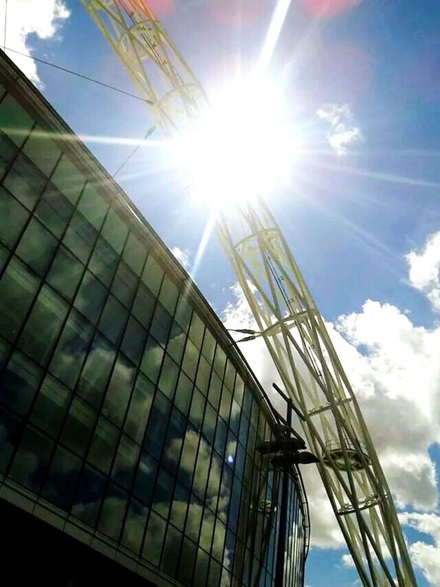 low angle view, sun, built structure, architecture, sunbeam, sunlight, sky, lens flare, building exterior, blue, reflection, sunny, bright, day, modern, tall - high, outdoors, cloud - sky, no people, glass - material