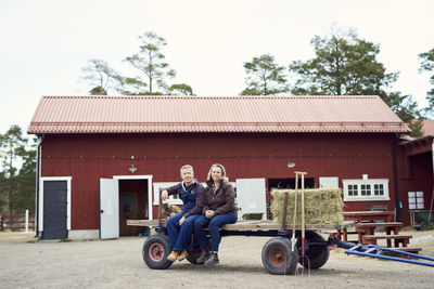 Mature couple sitting on old-fashioned trailer against barn