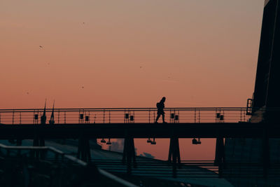 Silhouette people walking on bridge against orange sky