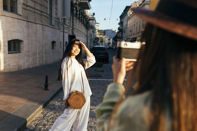 Female friend photographing woman through camera at city street