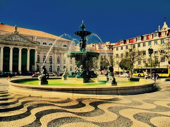 Fountain in city against clear blue sky