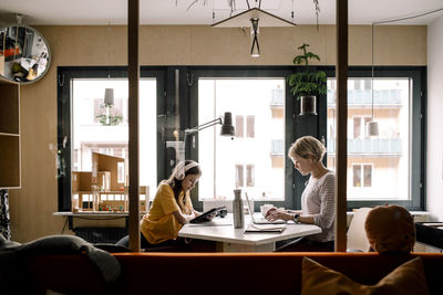 Female professional and daughter sitting at desk seen through glass