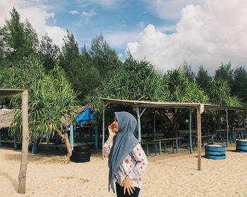 Young woman wearing hijab standing against trees