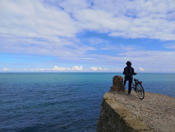 Rear view of man riding bicycle by sea against sky