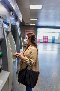 Woman wearing mask using atm at mall