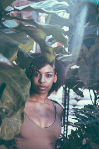 Portrait of young woman standing amidst plants on sunny day