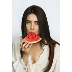 Portrait of young woman holding fruit against white background