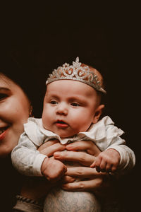 Portrait of young baby girl sitting against black background with her mom