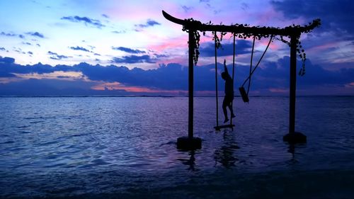 Silhouette wooden post in sea against sky at sunset