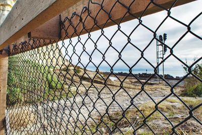 View of the beach through a chainlink fence against sky