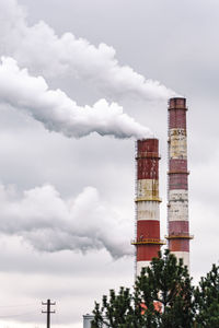 Thick white smoke from industrial factory old rusty chimneys on a cloudy grey sky background,