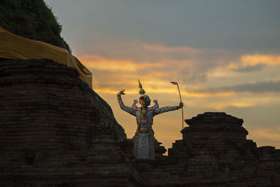 Man wearing traditional costume while standing on temple building against sky during sunset