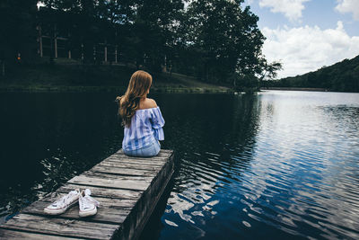 Rear view of woman sitting by lake against sky