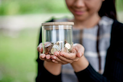 Midsection of woman holding glass jar with coins